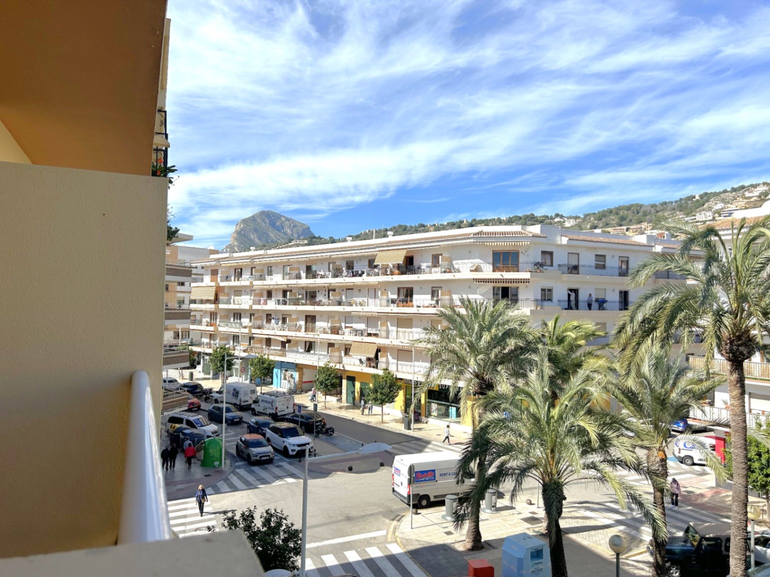 Vue dégagée depuis le balcon sur le centre du port de Jávea, avec la montagne emblématique du Montgó à l'horizon et des rues bordées de palmiers méditerranéens.