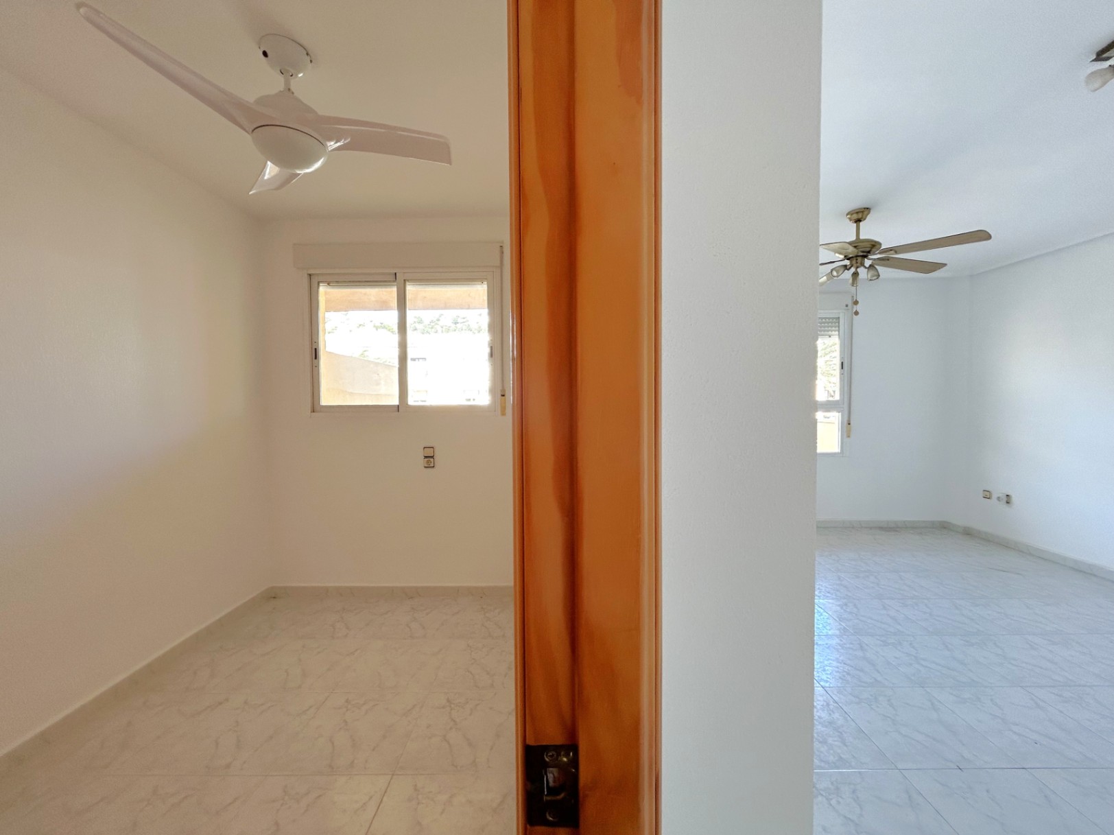 Vue intérieure de deux chambres adjacentes avec carrelage au sol, ventilateurs de plafond et menuiserie en bois naturel.