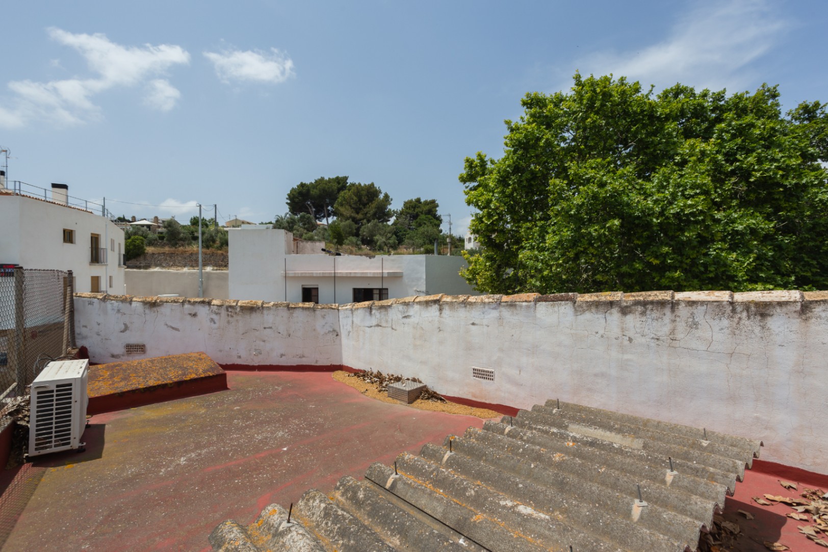 Terrasse de toit avec revêtement rouge et murs blancs, offrant une vue dégagée sur les bâtiments environnants et la végétation locale à Jávea.