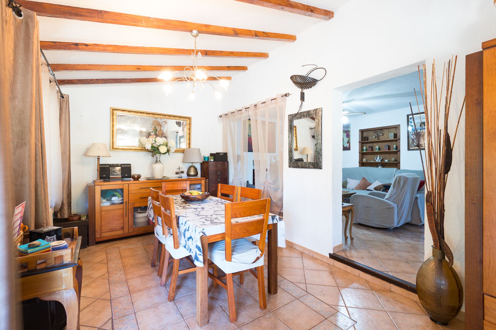 Salle à manger rustique avec poutres apparentes, sol en grès cérame et mobilier en bois massif, offrant une transition fluide vers le salon.