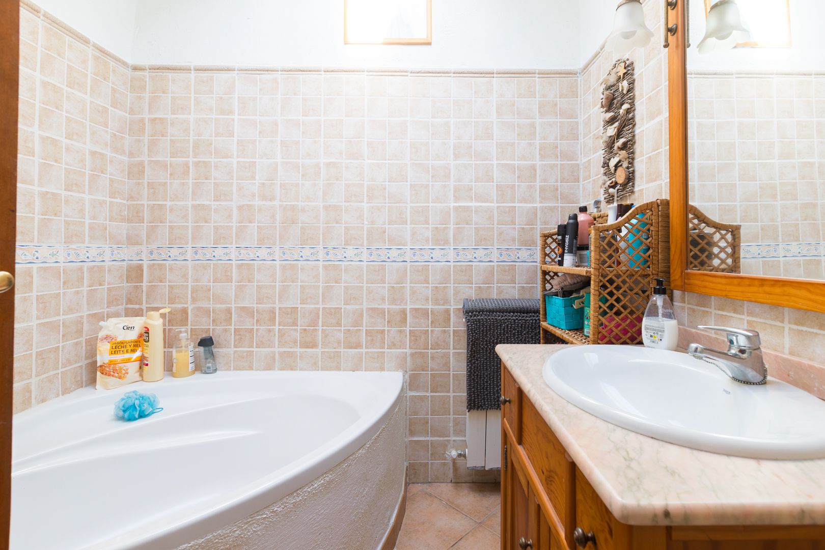 Salle de bain équipée d'une baignoire d'angle, d'un meuble vasque en bois avec plan en marbre et de murs carrelés dans des tons beige.