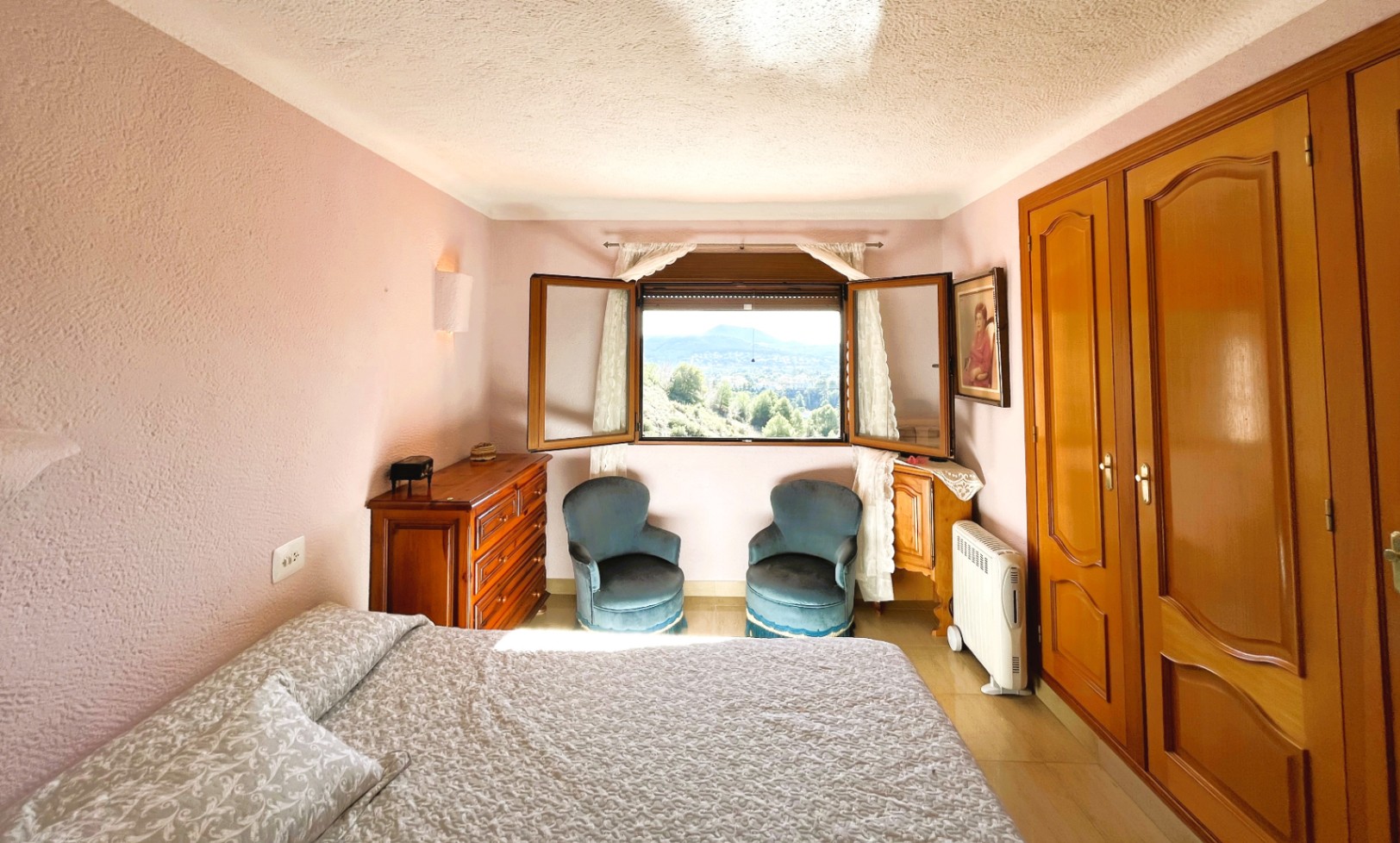 Chambre aux murs mauves texturés, avec placards intégrés en bois et une fenêtre offrant une vue panoramique sur la vallée environnante.