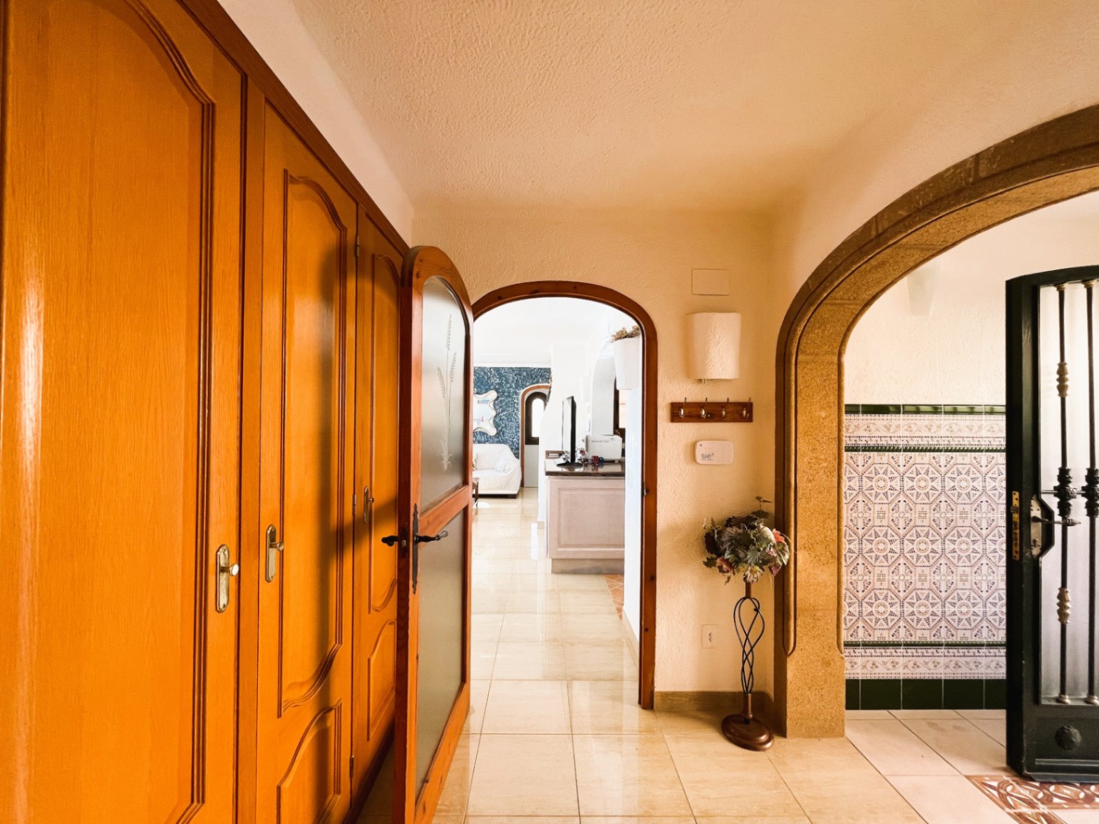Couloir d'entrée avec placards intégrés en bois, sol en grès poli et arches élégantes menant au salon et à un espace orné de carreaux de style traditionnel.