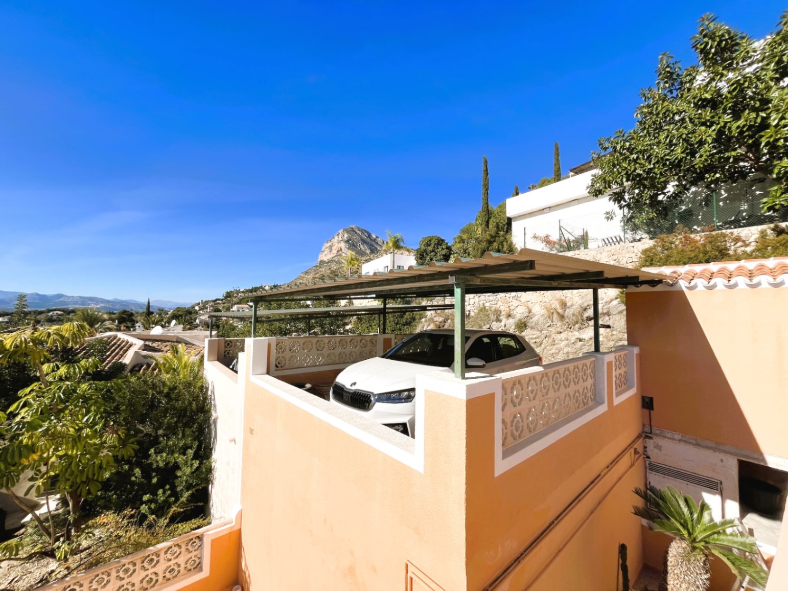 Espace de stationnement surélevé avec pergola métallique et garde-corps décoratif, offrant une vue dégagée sur le Montgó et la nature environnante.
