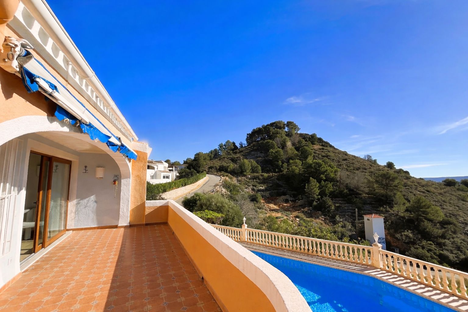 Terrasse supérieure avec carrelage en terre cuite, store banne et vue panoramique sur les collines environnantes et la piscine.