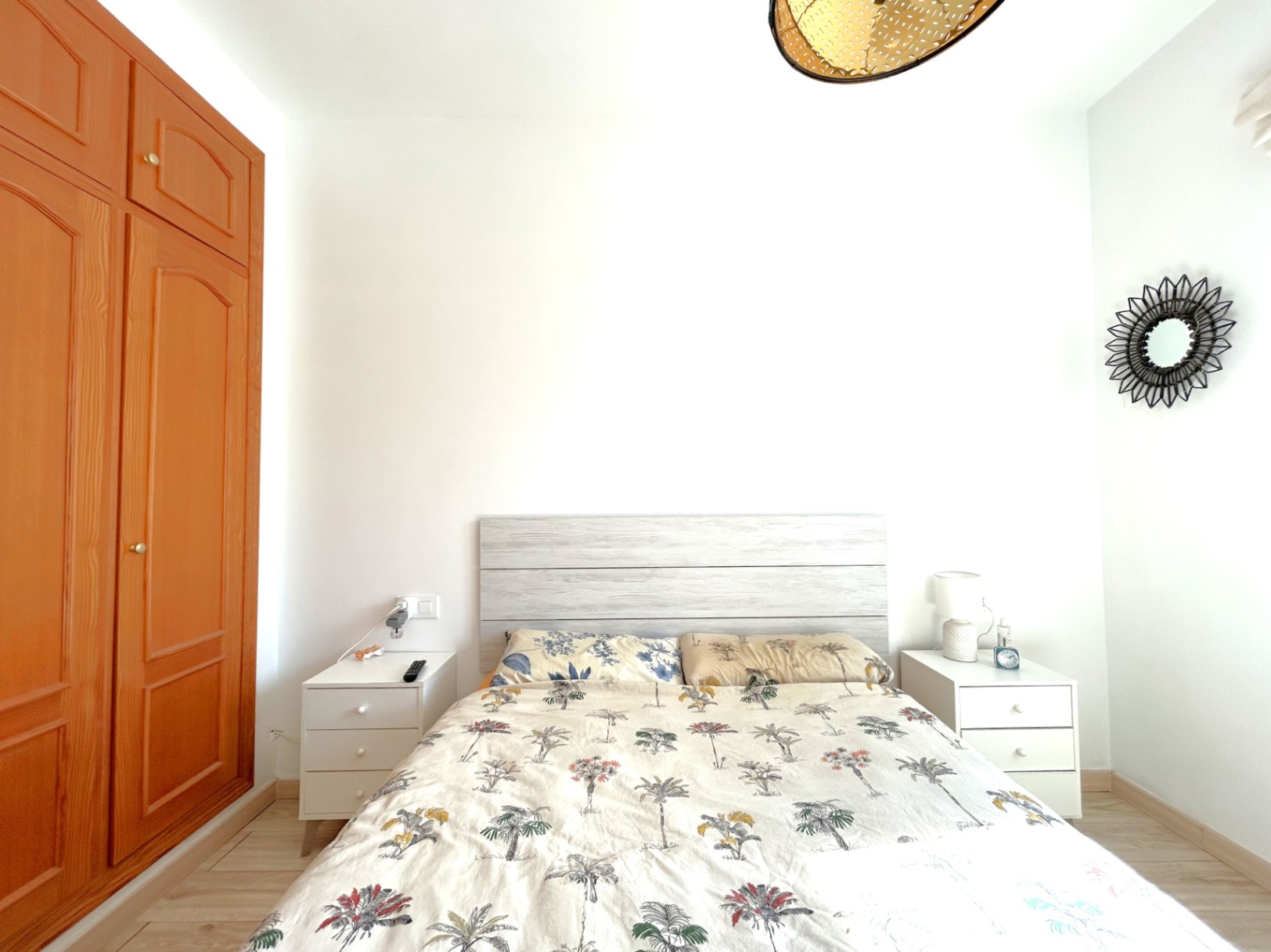 Chambre double avec armoire encastrée en bois, tables de chevet blanches et tête de lit en bois clair. La pièce dispose d'un sol stratifié et d'une lumière naturelle.