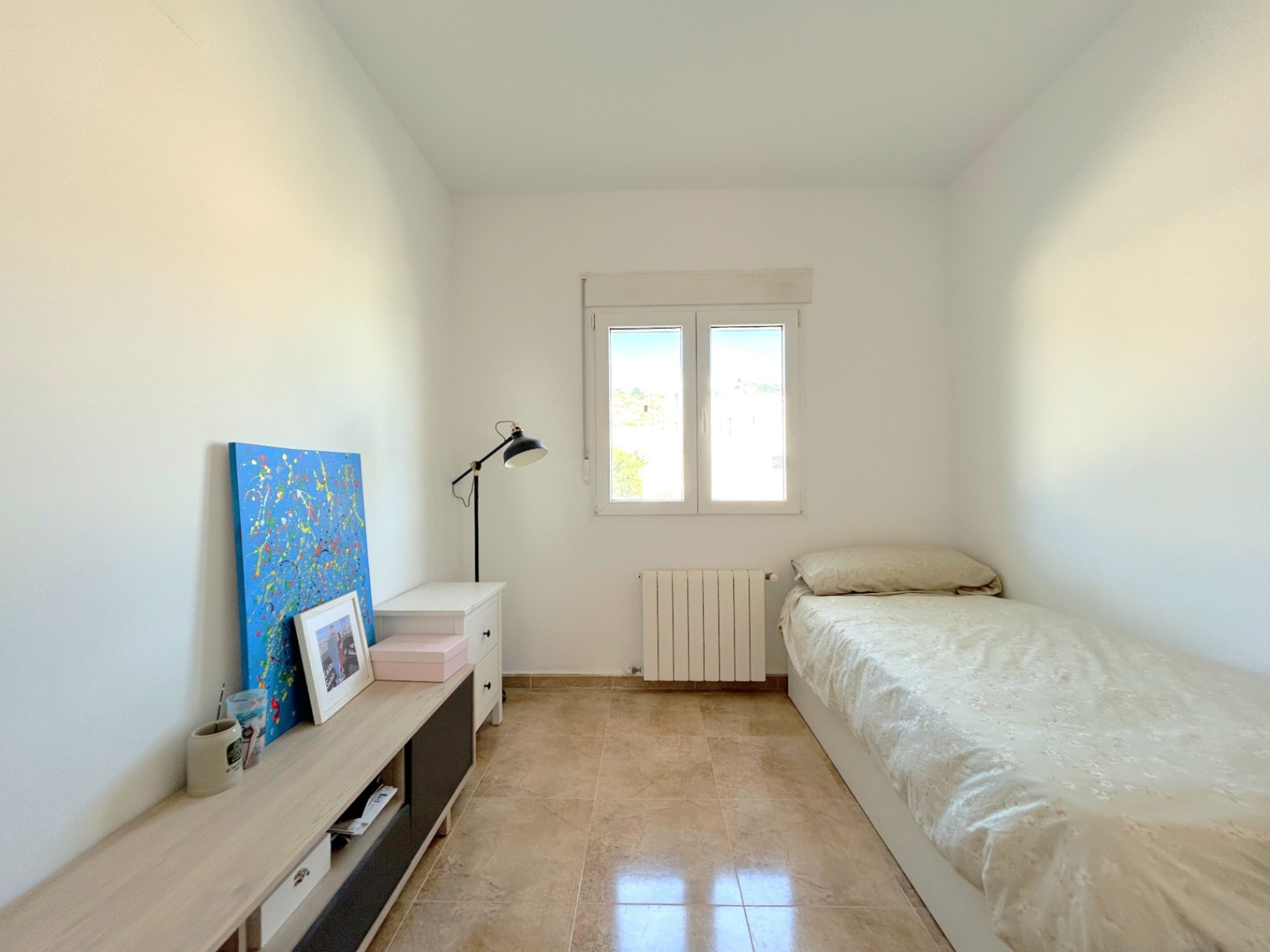 Chambre lumineuse avec sol en grès, radiateur de chauffage central et fenêtre à double vitrage offrant une belle luminosité naturelle.