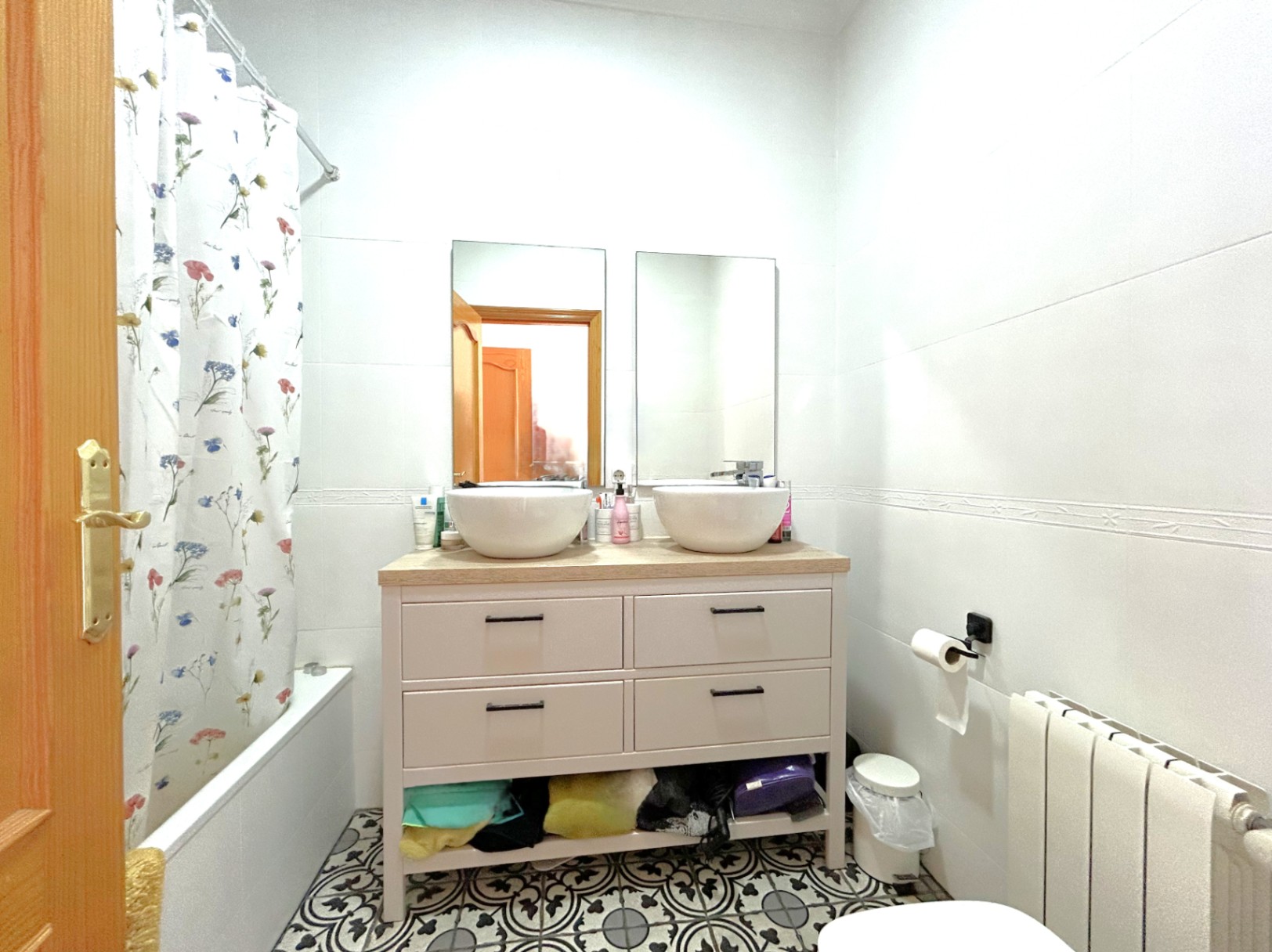Salle de bain avec double vasque sur plan de travail en bois, sol en carreaux de ciment décoratifs, baignoire et radiateur de chauffage central.