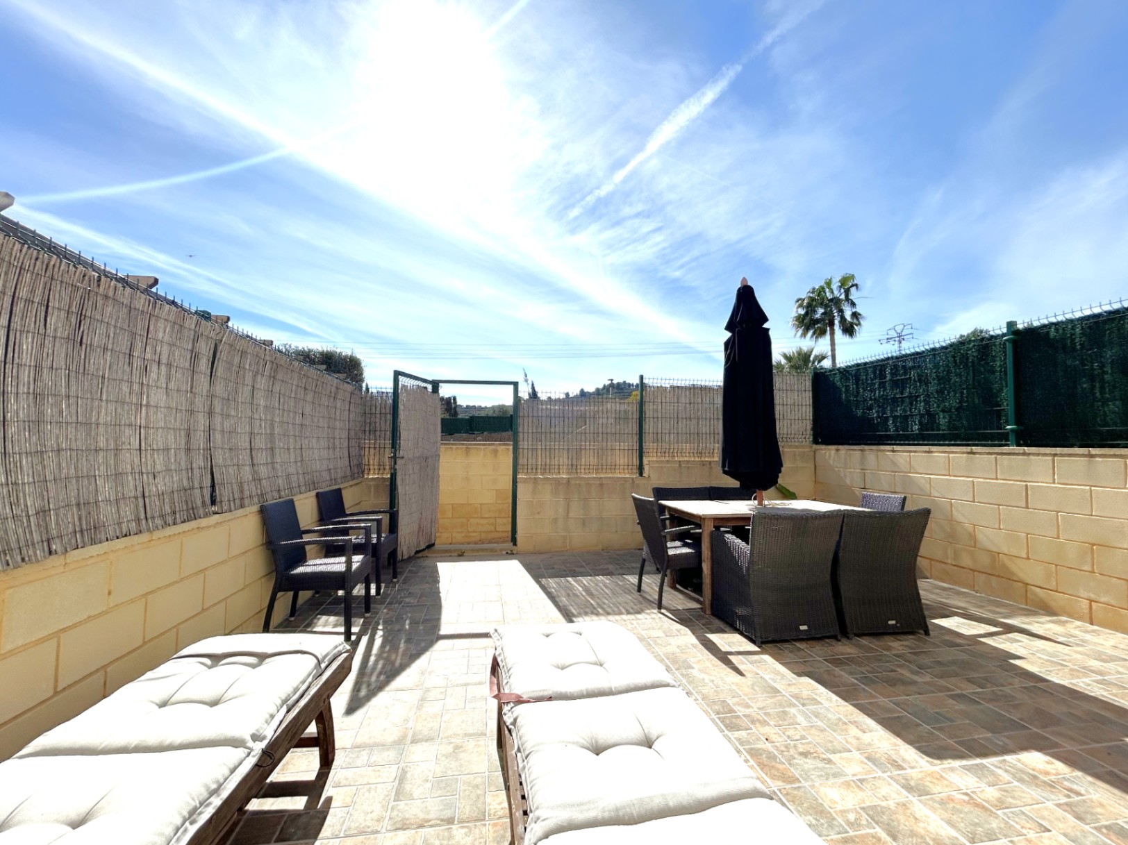 Terrasse privée orientée plein sud avec sol en grès, comprenant un coin repas extérieur, des bains de soleil et une clôture en brande pour l'intimité.