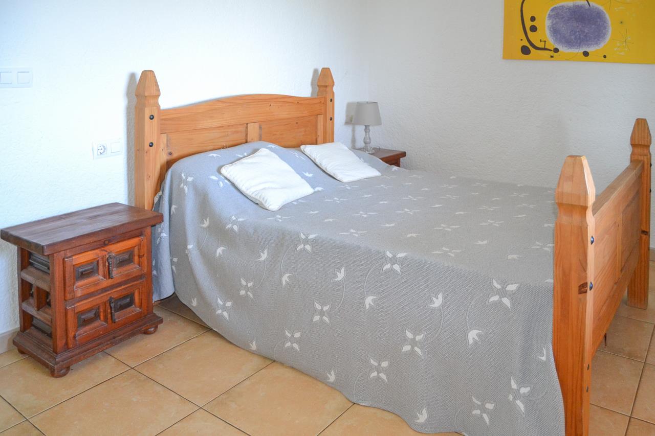Chambre à coucher avec cadre de lit en bois rustique, tables de chevet assorties et sol en grès. Les murs blancs apportent de la clarté à la pièce.