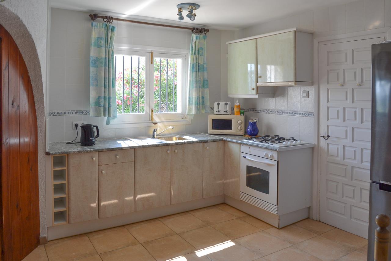 Cuisine fonctionnelle avec placards crème, plan de travail effet granit et équipements incluant four blanc et plaque de cuisson, éclairée par une fenêtre.