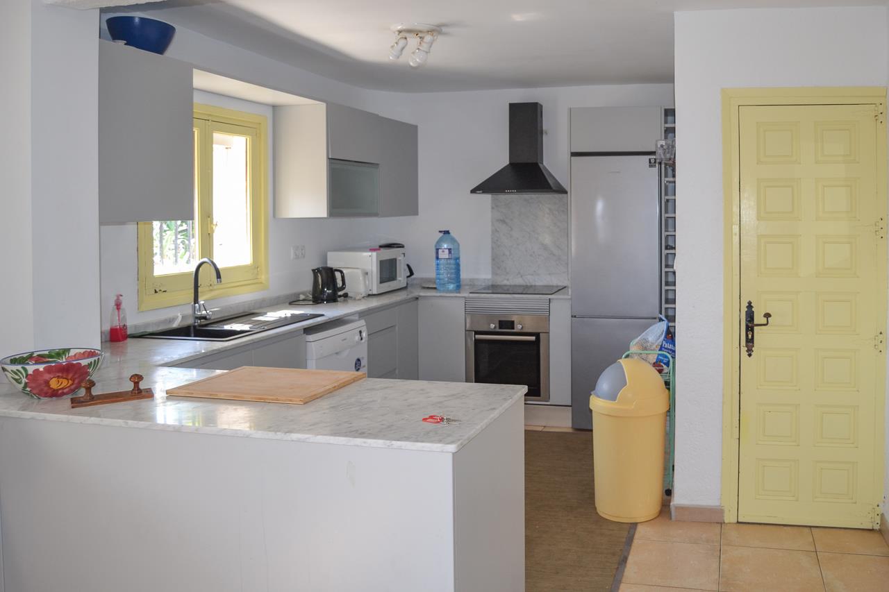 Cuisine fonctionnelle avec placards gris, plans de travail en marbre et électroménager intégré. Les menuiseries jaunes apportent une touche de couleur à cet espace pratique.