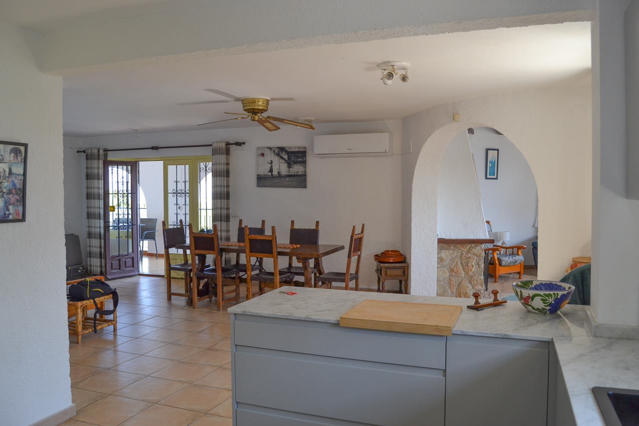 Cuisine ouverte avec plans de travail en marbre donnant sur un coin repas. Comprend la climatisation, un ventilateur de plafond et un accès direct à la terrasse.