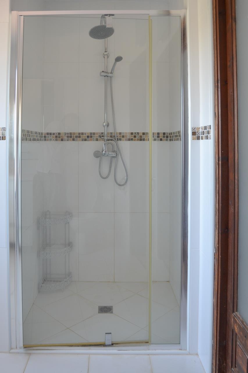 Douche à l'italienne moderne avec paroi en verre, pommeau à effet pluie et frise décorative en mosaïque sur carrelage blanc.