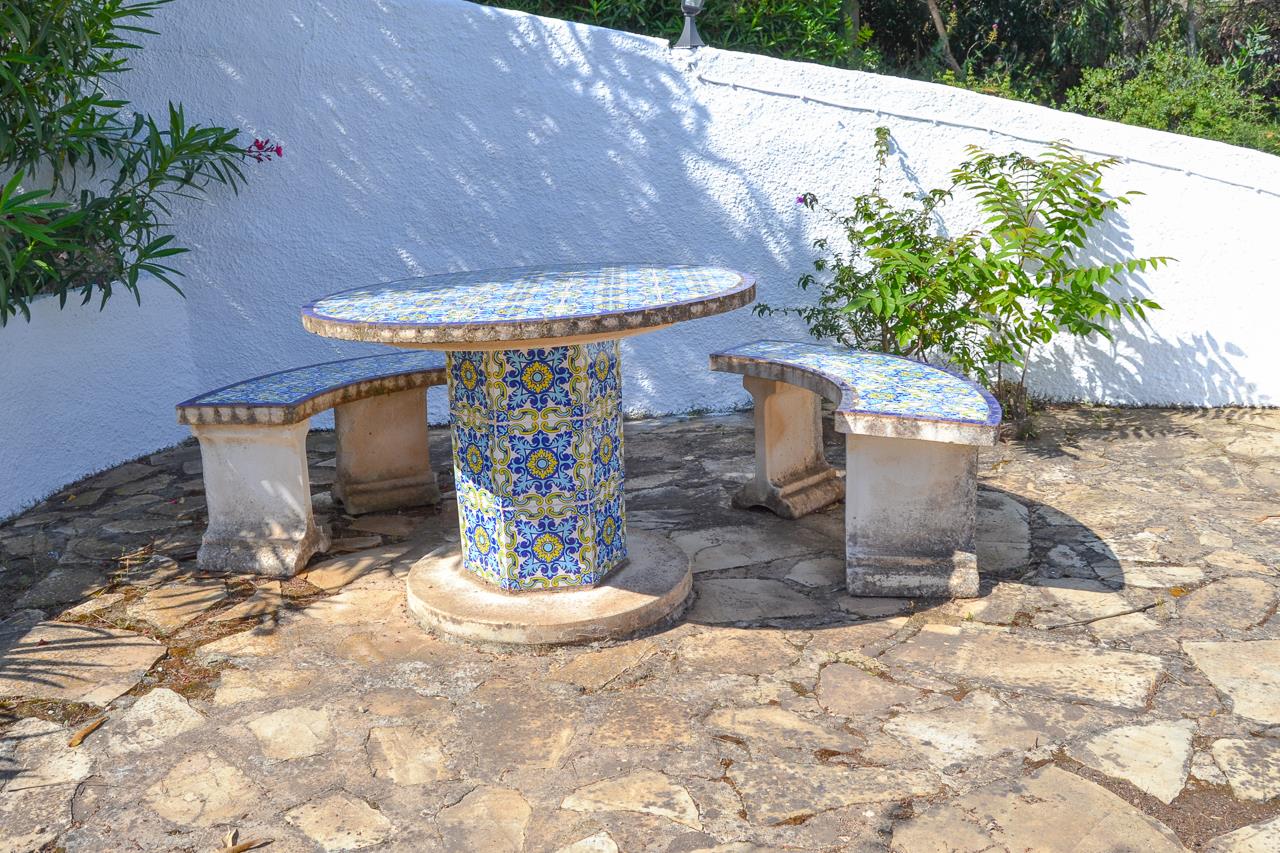 Espace de détente extérieur avec table et bancs incurvés ornés de faïences traditionnelles, disposés sur une terrasse en pierre naturelle.