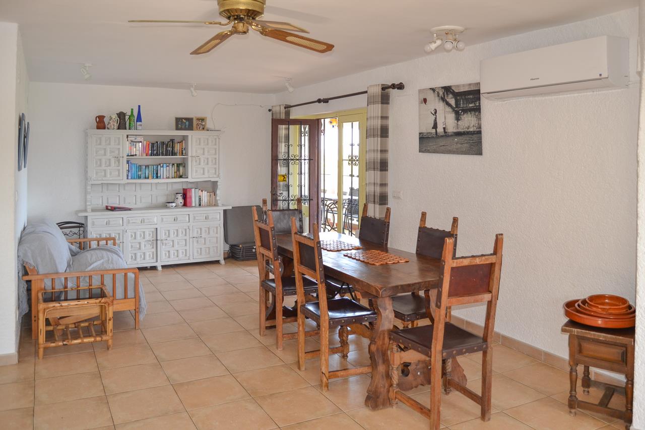 Espace salle à manger avec table en bois massif, chaises rustiques et buffet blanc. Équipé d'un ventilateur de plafond, de la climatisation et d'un accès vers la terrasse extérieure.
