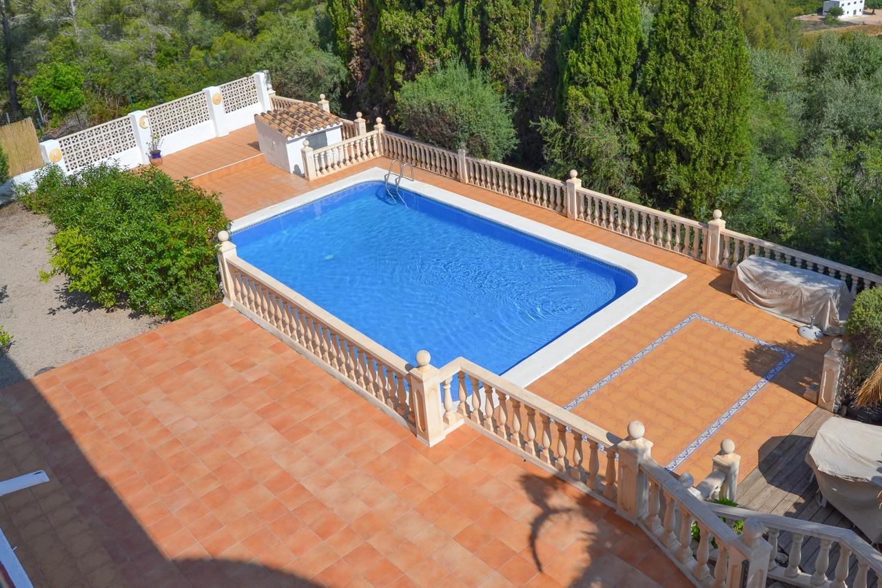 Grande piscine rectangulaire entourée d'une terrasse en terre cuite et d'une balustrade en pierre classique, située au cœur d'un jardin méditerranéen arboré.