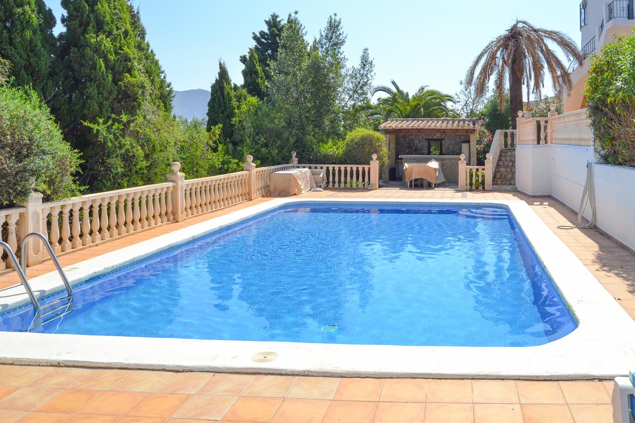 Piscine de 12x6m avec mosaïque bleue, vaste terrasse en terre cuite, balustrades en pierre et cuisine d'été couverte avec bar dans un cadre verdoyant.