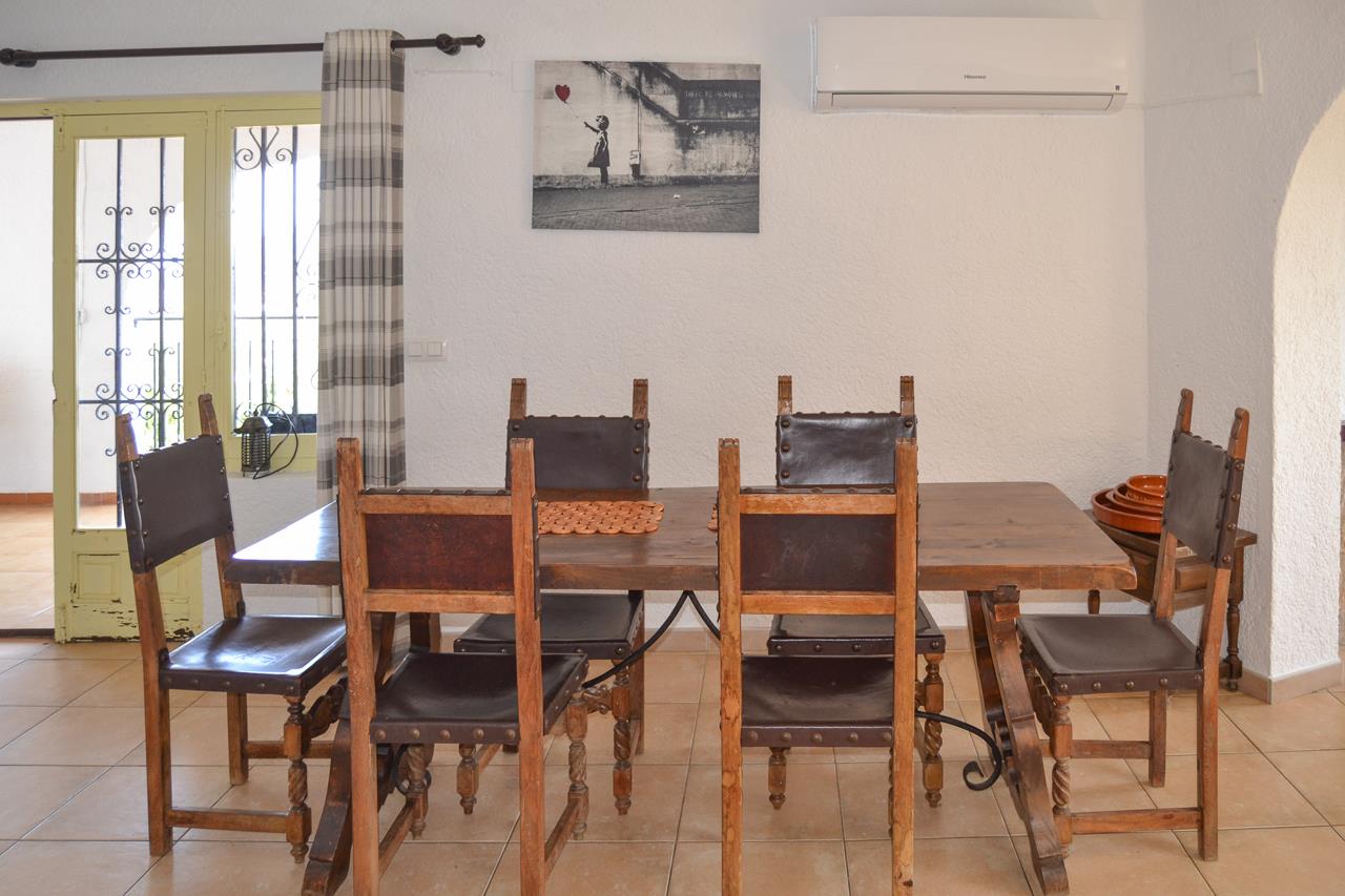 Salle à manger rustique avec table en bois massif et chaises en cuir. Équipée de la climatisation, de sols en grès et d'une porte avec ferronnerie décorative.