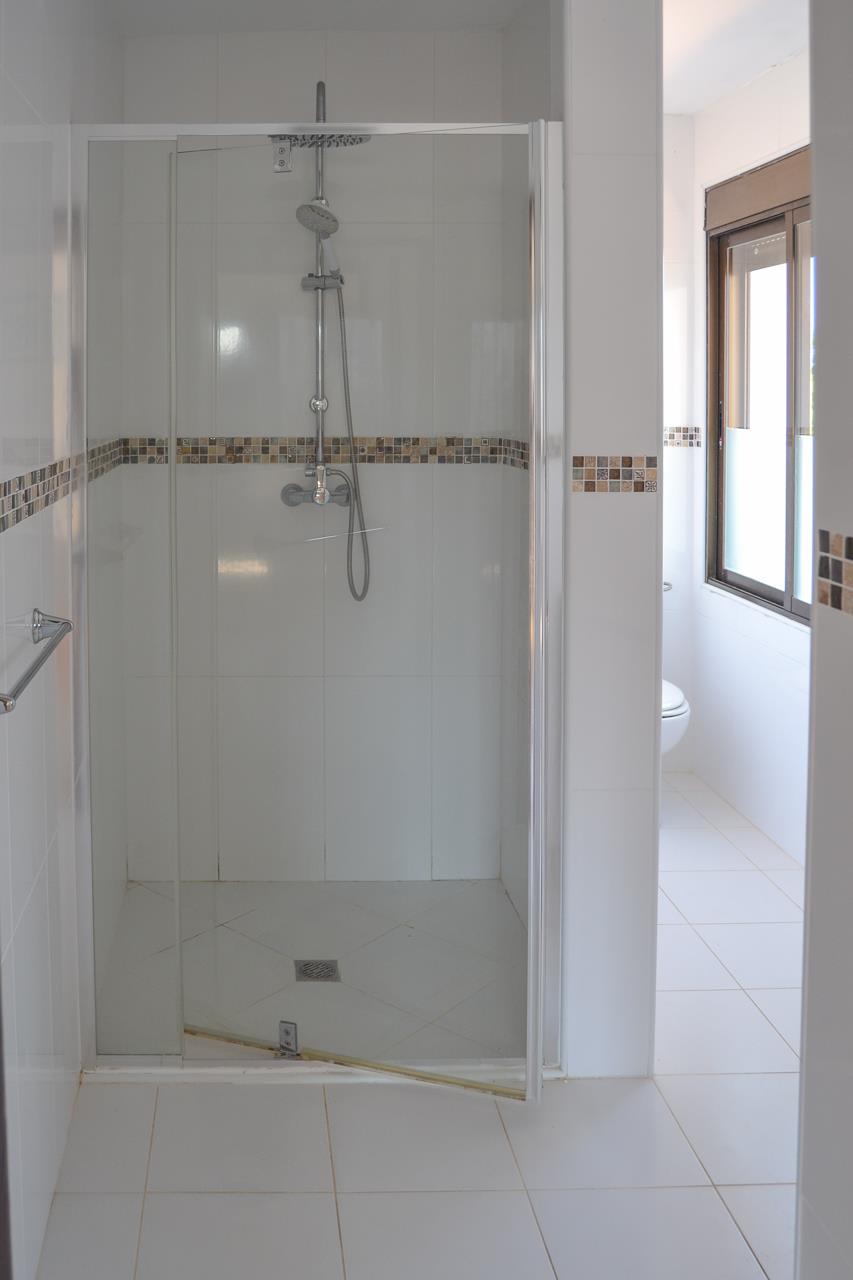 Salle de bain avec douche à l'italienne, paroi en verre, carrelage blanc et frise décorative en mosaïque aux tons terreux.