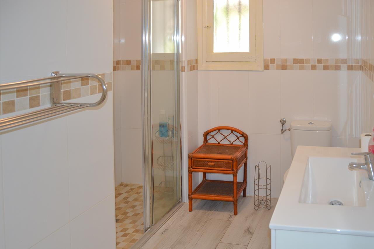 Salle de bain fonctionnelle avec douche à l'italienne, paroi vitrée et meuble vasque blanc. Les murs sont carrelés avec une frise décorative élégante.