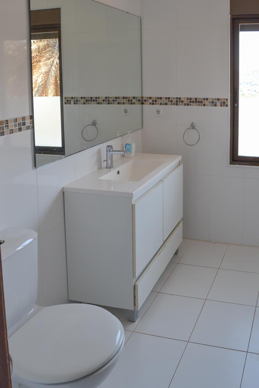 Salle de bains avec meuble vasque blanc, grand miroir et carrelage mural orné d'une frise en mosaïque. La fenêtre apporte une luminosité naturelle.