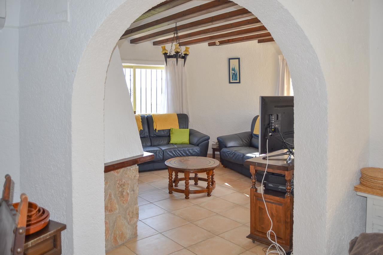 Salon rustique aperçu à travers une arche, avec poutres apparentes au plafond, canapés en cuir sombre et sol en carrelage traditionnel.