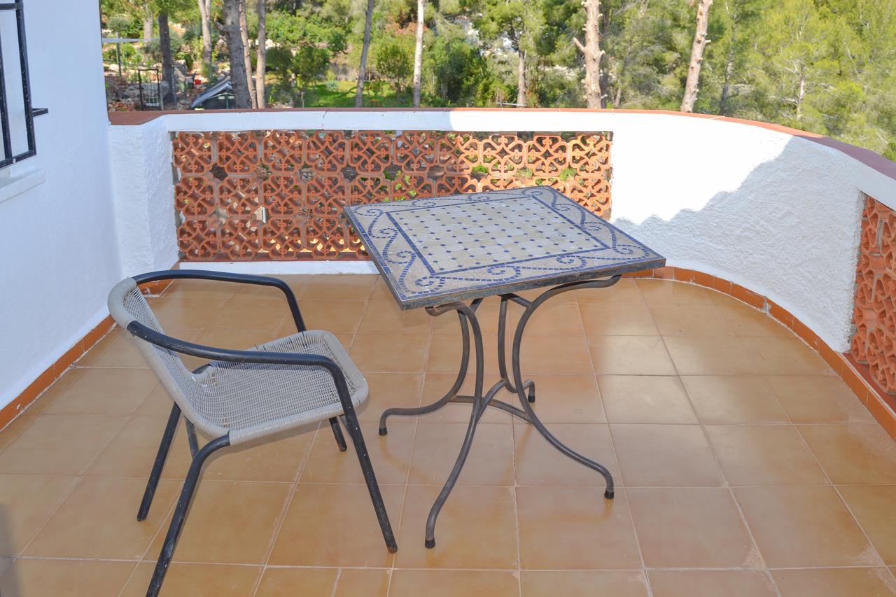 Terrasse avec carrelage en terre cuite, table en mosaïque bleue et balustrade en terre cuite ajourée offrant une vue sur la pinède environnante.