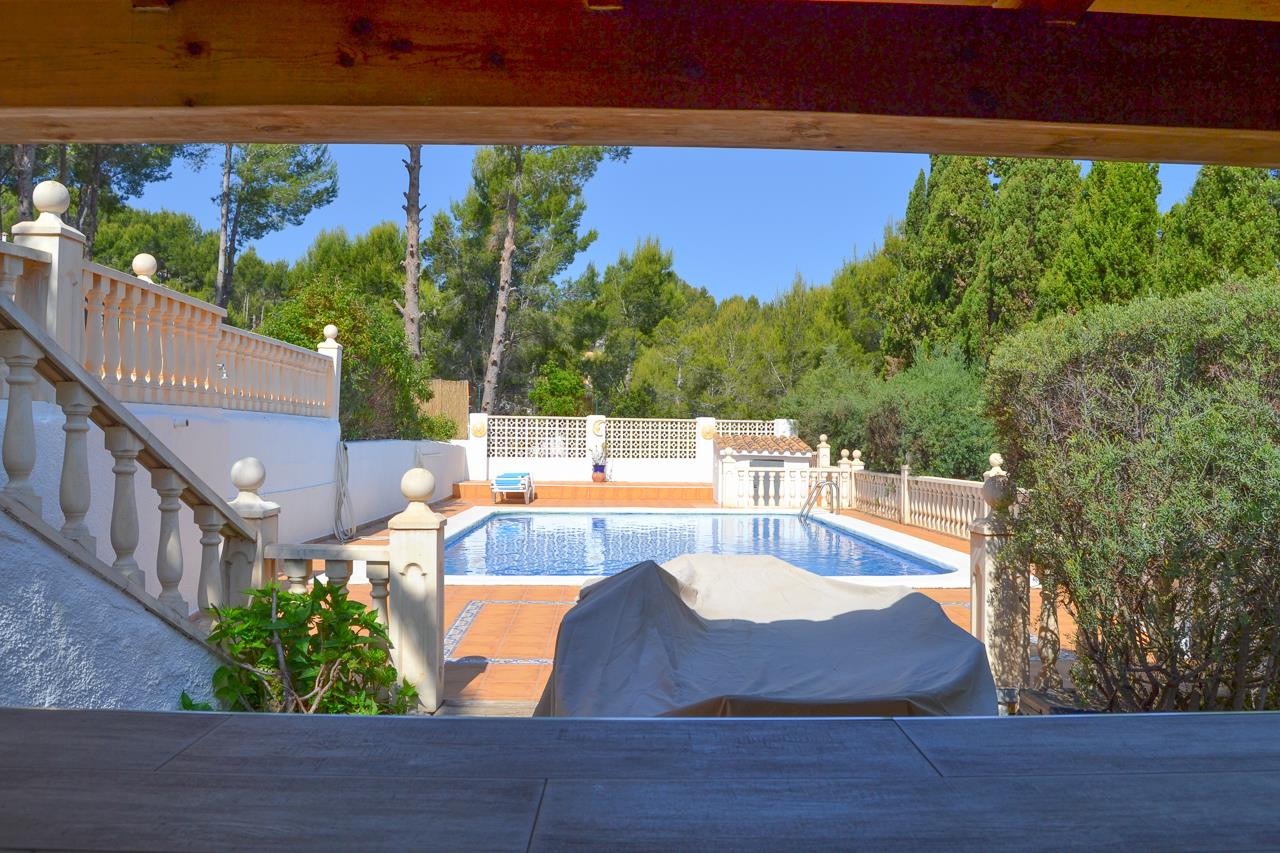Vue depuis le bar couvert sur la piscine privée, entourée de terrasses en terre cuite, de balustrades blanches et d'une végétation méditerranéenne dense.