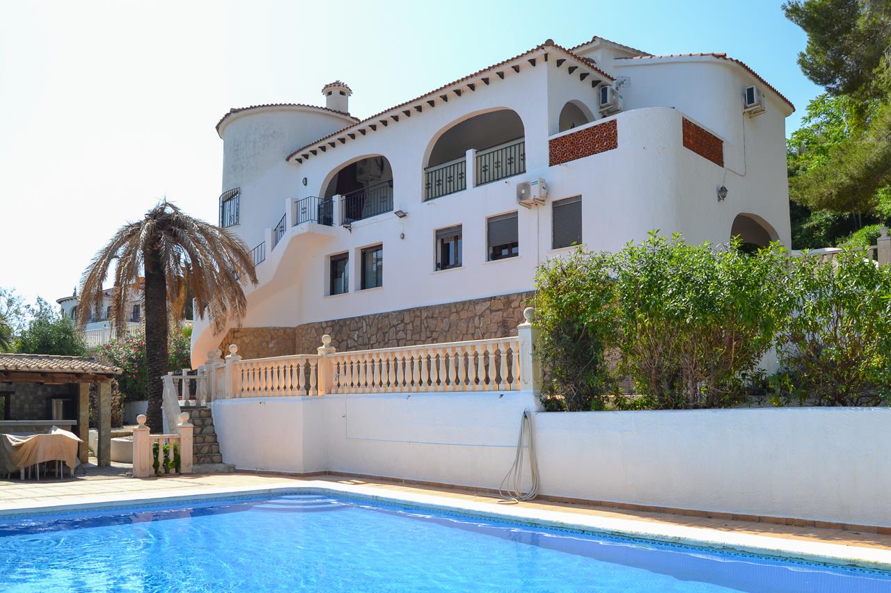 Vue extérieure de la villa avec piscine privée, façades blanches méditerranéennes et terrasses couvertes en arches sur un soubassement en pierre naturelle.