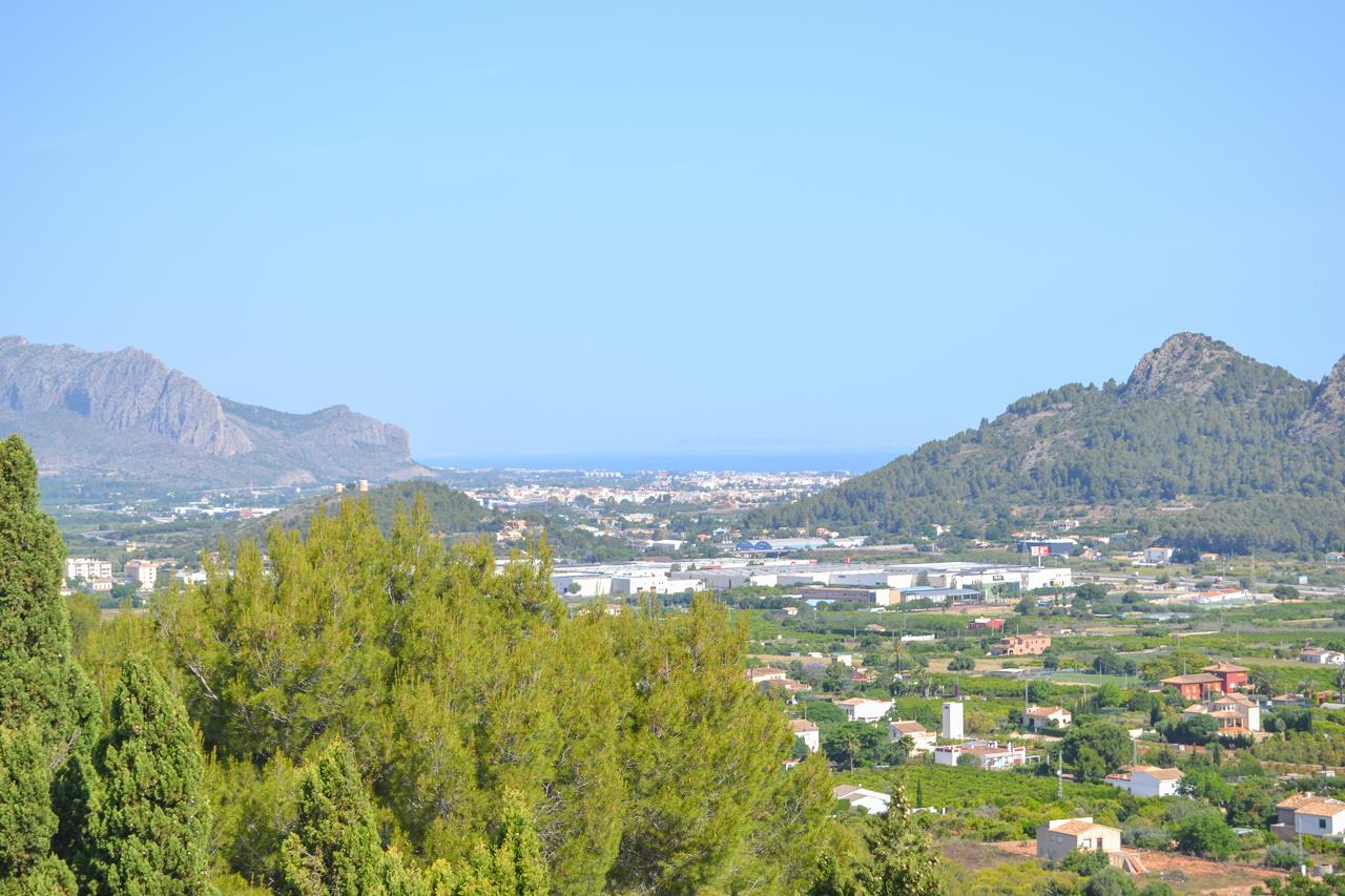 Vues panoramiques dégagées sur la vallée et la mer Méditerranée, encadrées par des montagnes et une végétation de pins sous un ciel bleu clair.