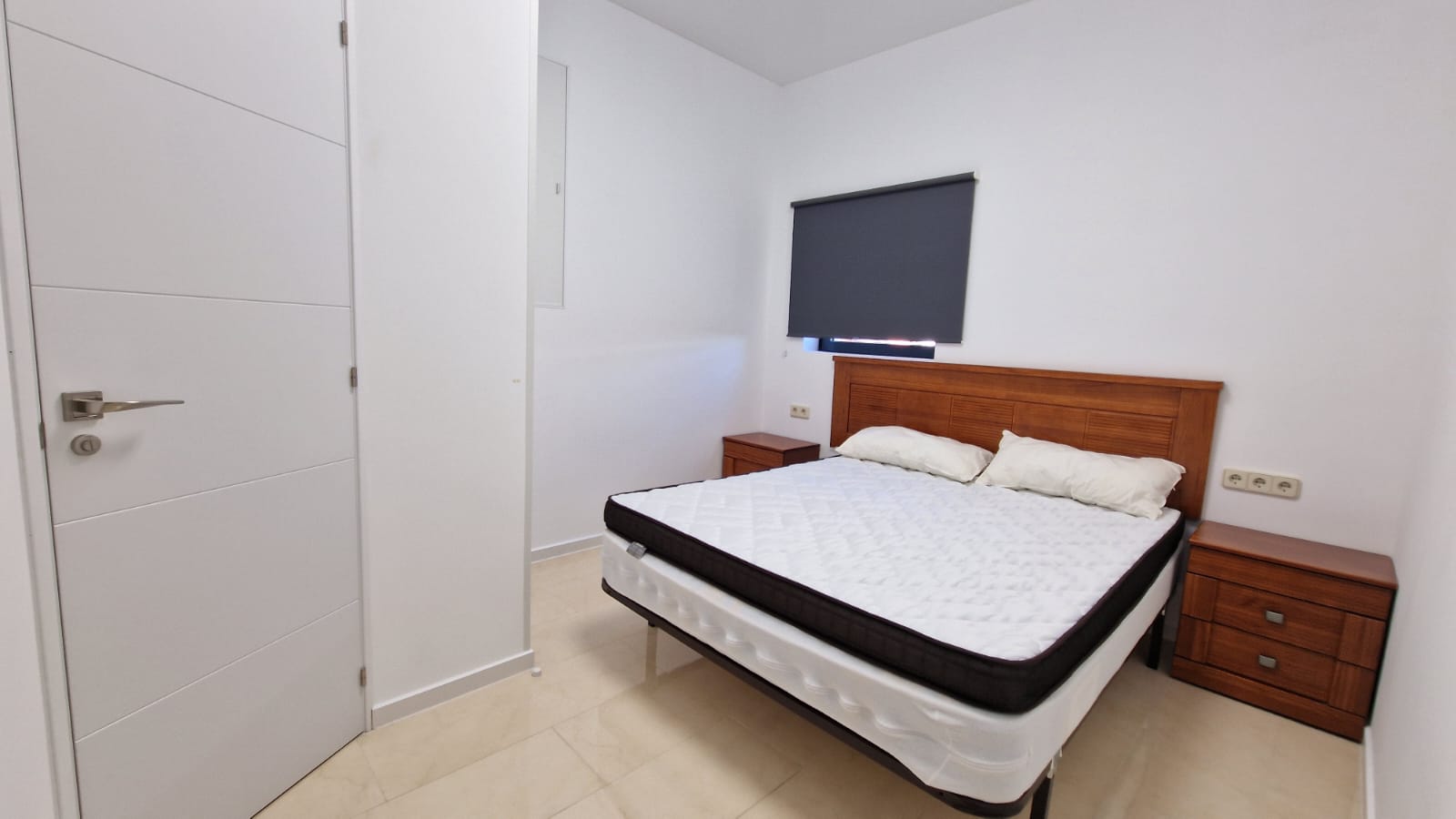 Chambre lumineuse avec lit double, tables de chevet en bois et porte blanche au design moderne.