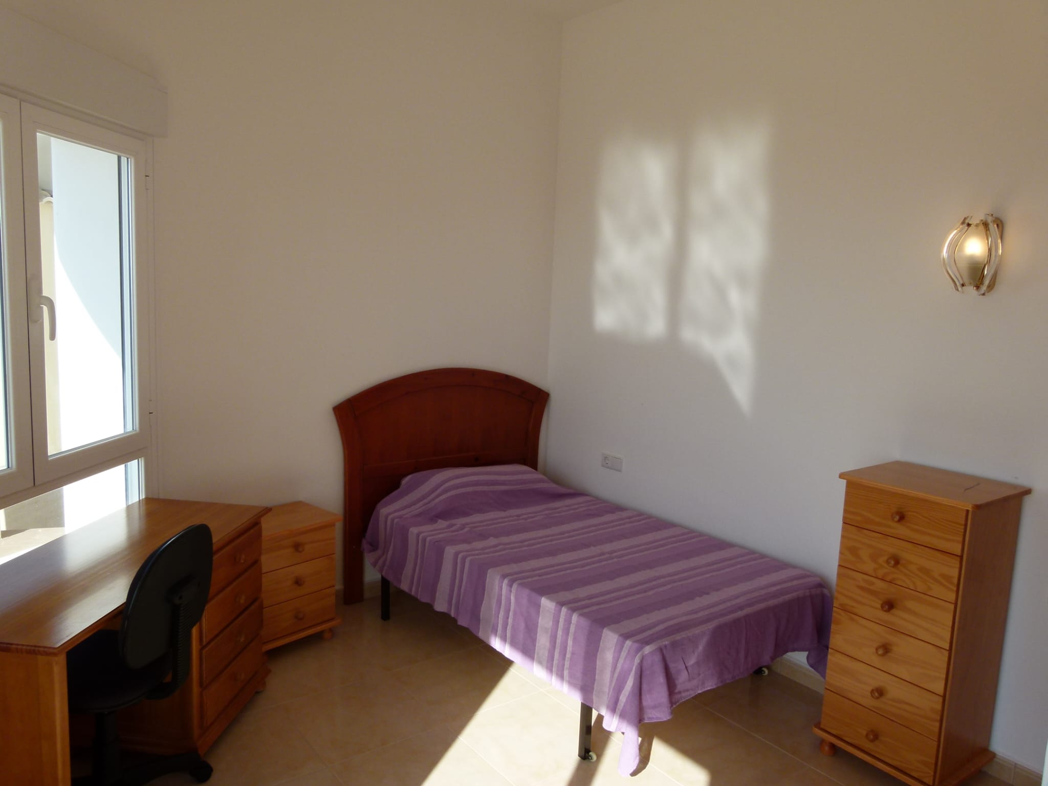 Chambre lumineuse avec lit simple, bureau en bois et commode assortie.