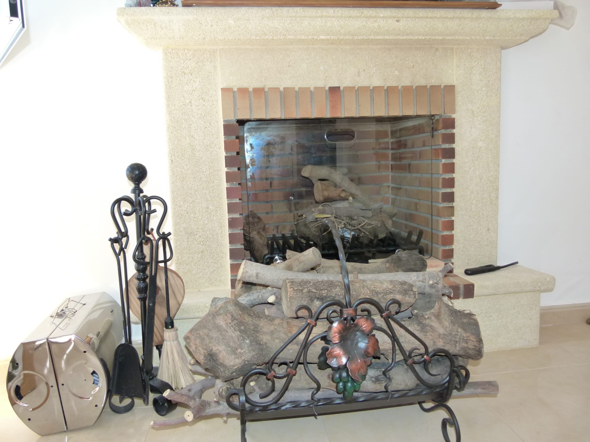 Cheminée en brique avec accessoires en fer forgé et bois de chauffage empilé sur un support décoratif.