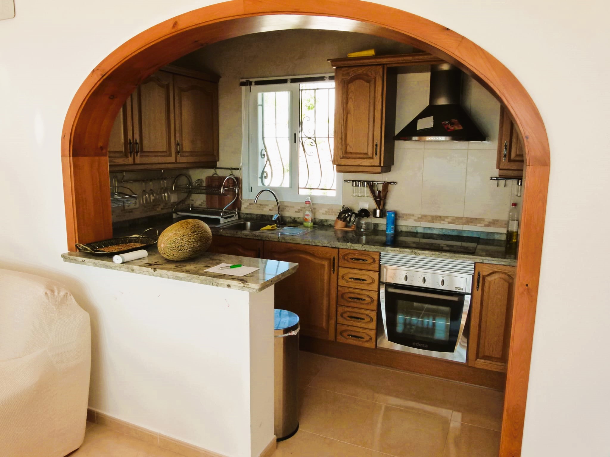 Cuisine avec arche en bois, meubles couleur miel et plans de travail en granit. Style rustique et fonctionnel.