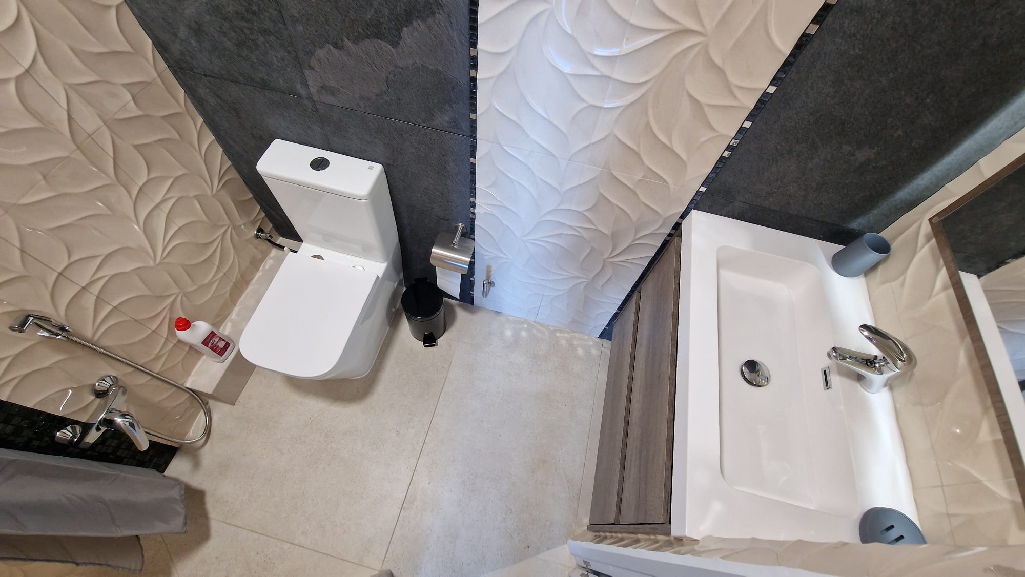 Détail de salle de bain avec carrelage texturé, toilette blanche et lavabo moderne. Design fonctionnel et élégant.