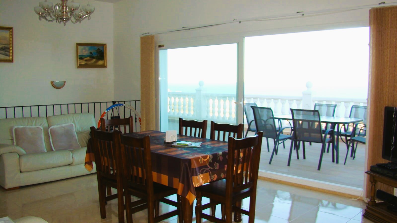 Salle à manger lumineuse avec table en bois et accès à la terrasse avec vue sur la mer.
