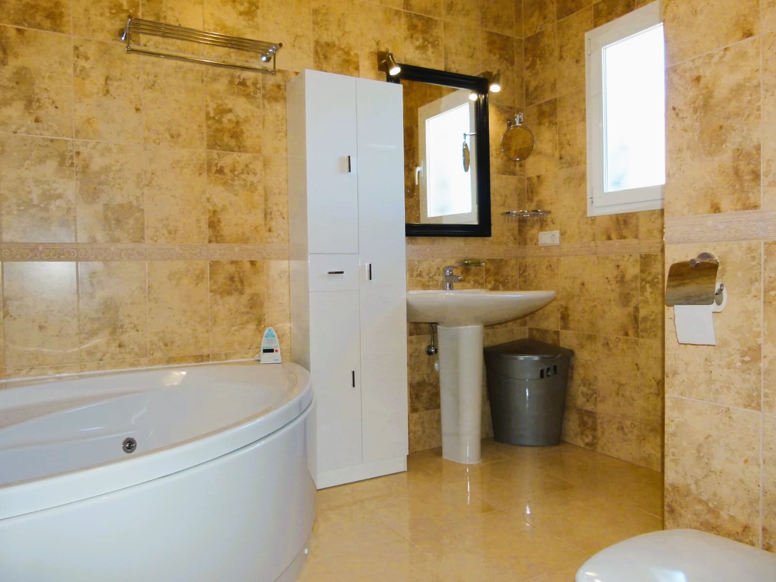 Salle de bain avec baignoire ronde, lavabo sur colonne et carrelage beige.