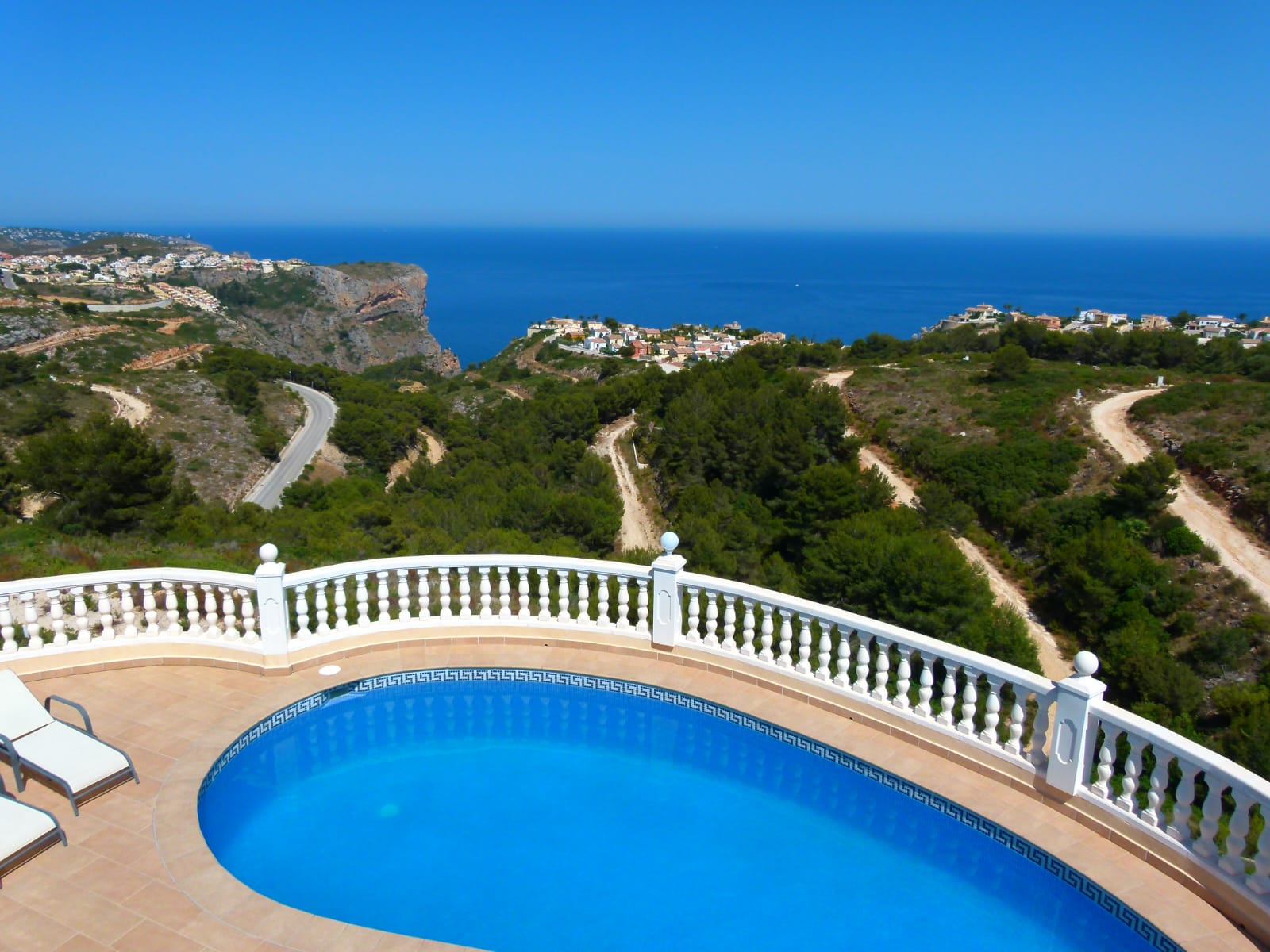 Vue sur la piscine privée avec rambarde blanche et vue panoramique sur la côte et la végétation.