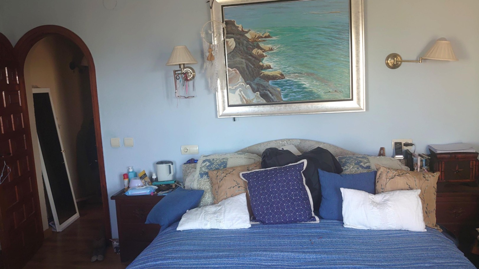 Chambre aux murs bleu clair avec un grand tableau marin, des appliques murales classiques et une porte cintrée en bois massif.