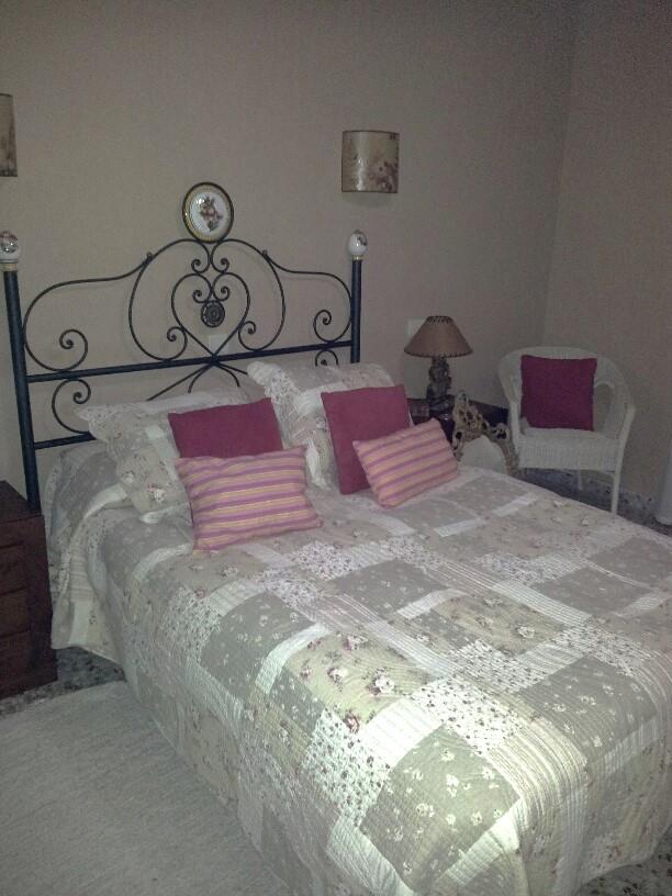 Chambre avec tête de lit en fer forgé, couvre-lit en patchwork et fauteuil en osier blanc. Éclairage par appliques murales et lampe de chevet traditionnelle.