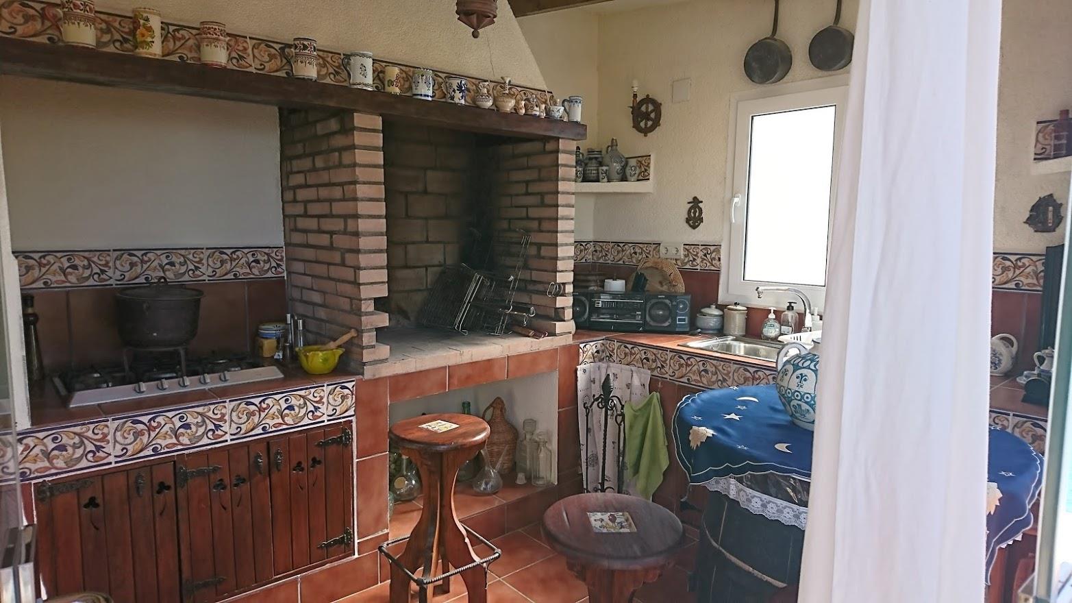 Cuisine d'été rustique avec barbecue en briques, plan de travail en carrelage traditionnel, meubles en bois et évier lumineux.