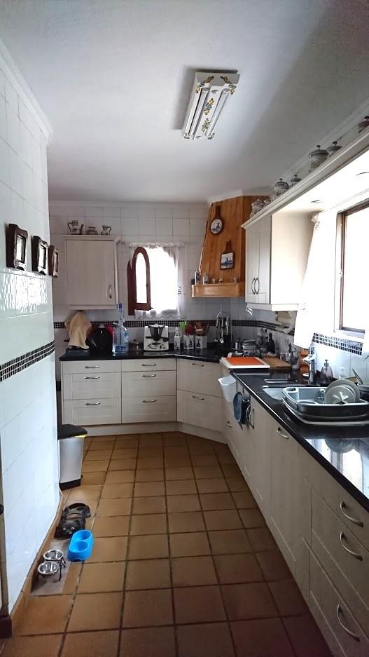 Cuisine indépendante avec placards blancs, plan de travail sombre et sol en terre cuite. Elle dispose d'une hotte en bois et de murs carrelés avec frise décorative.