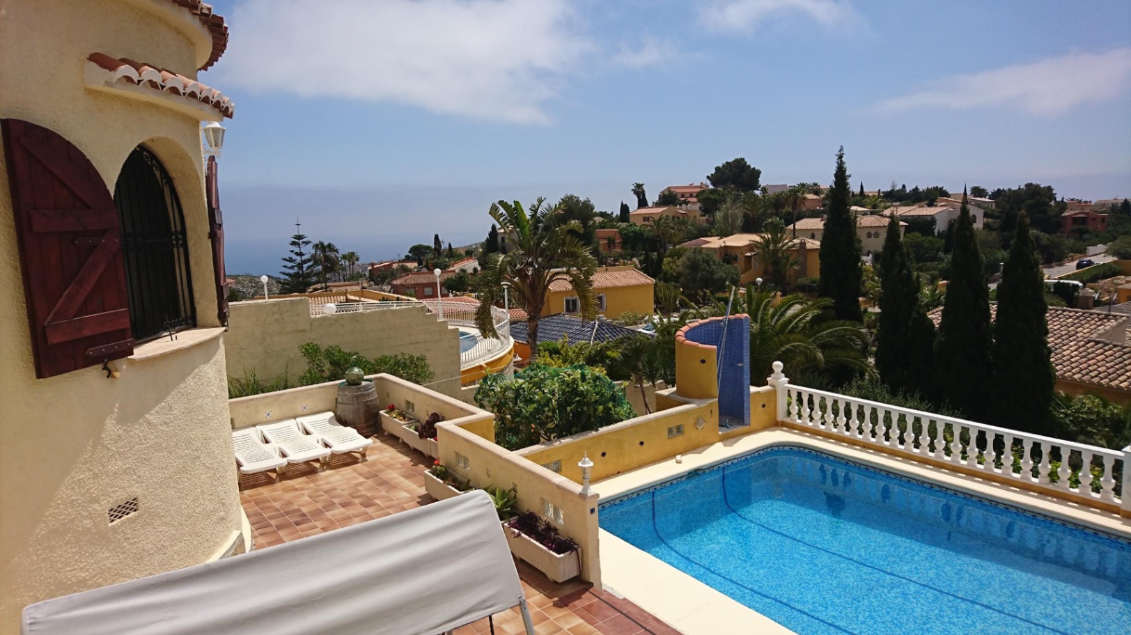 Espace extérieur avec piscine rectangulaire, terrasse en terre cuite, balustrades blanches et tour provençale avec volets en bois offrant une vue dégagée sur la mer.