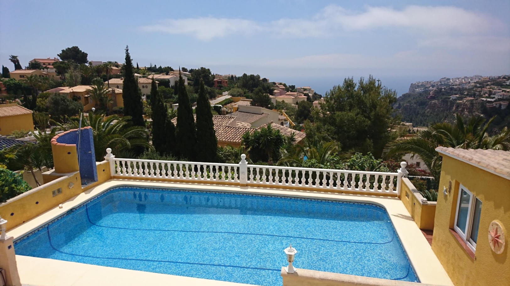 Piscine rectangulaire avec revêtement en mosaïque bleue, entourée d'une balustrade blanche classique offrant une vue dégagée sur la mer Méditerranée.
