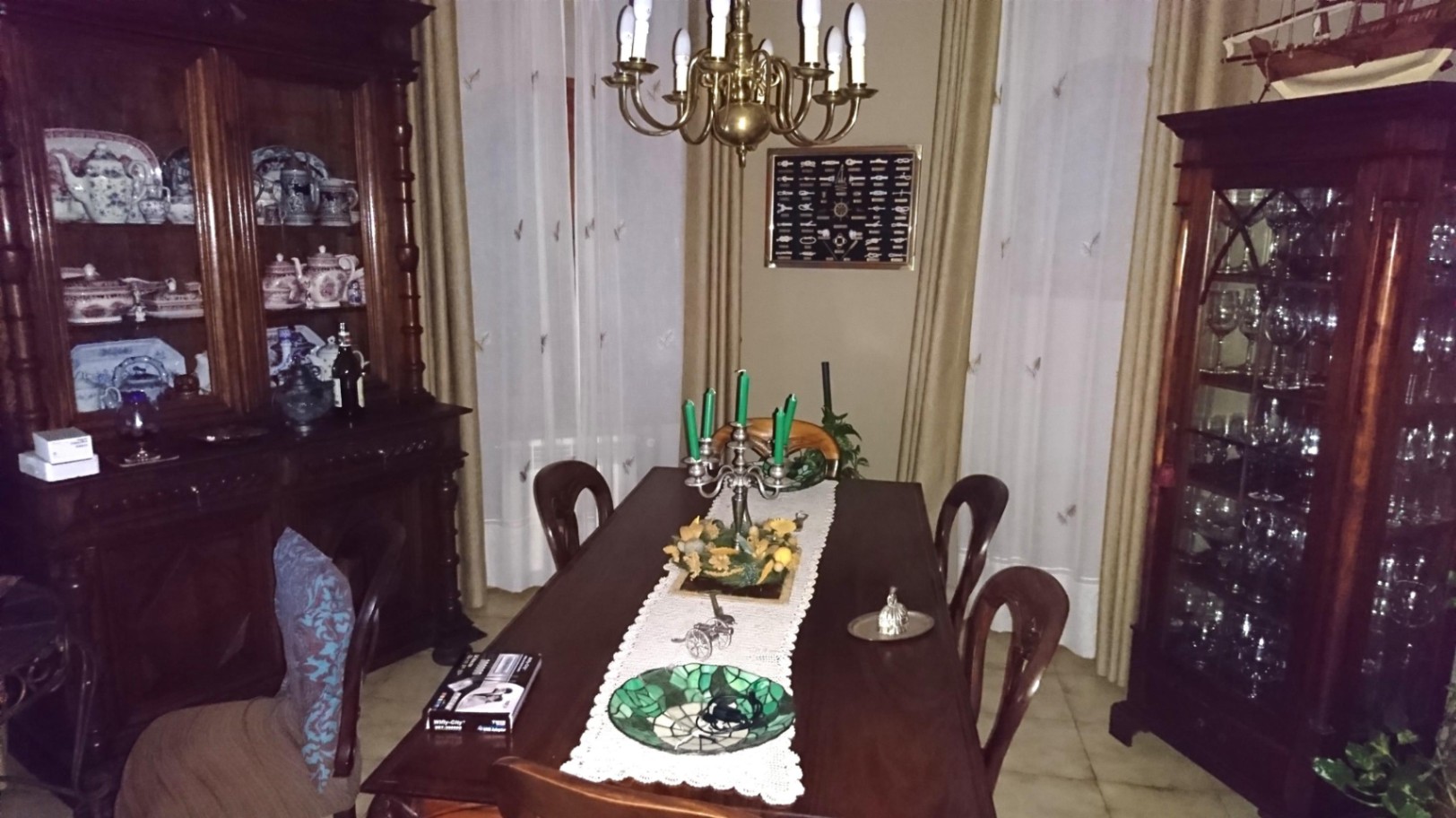 Salle à manger classique avec table en bois sombre, vaisseliers sculptés et lustre en laiton, complétée par des rideaux aux tons neutres.
