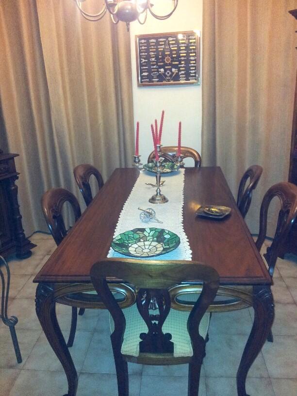 Salle à manger formelle avec table en bois sombre, chaises classiques assorties et rideaux beiges. Le sol est revêtu de carrelage clair.