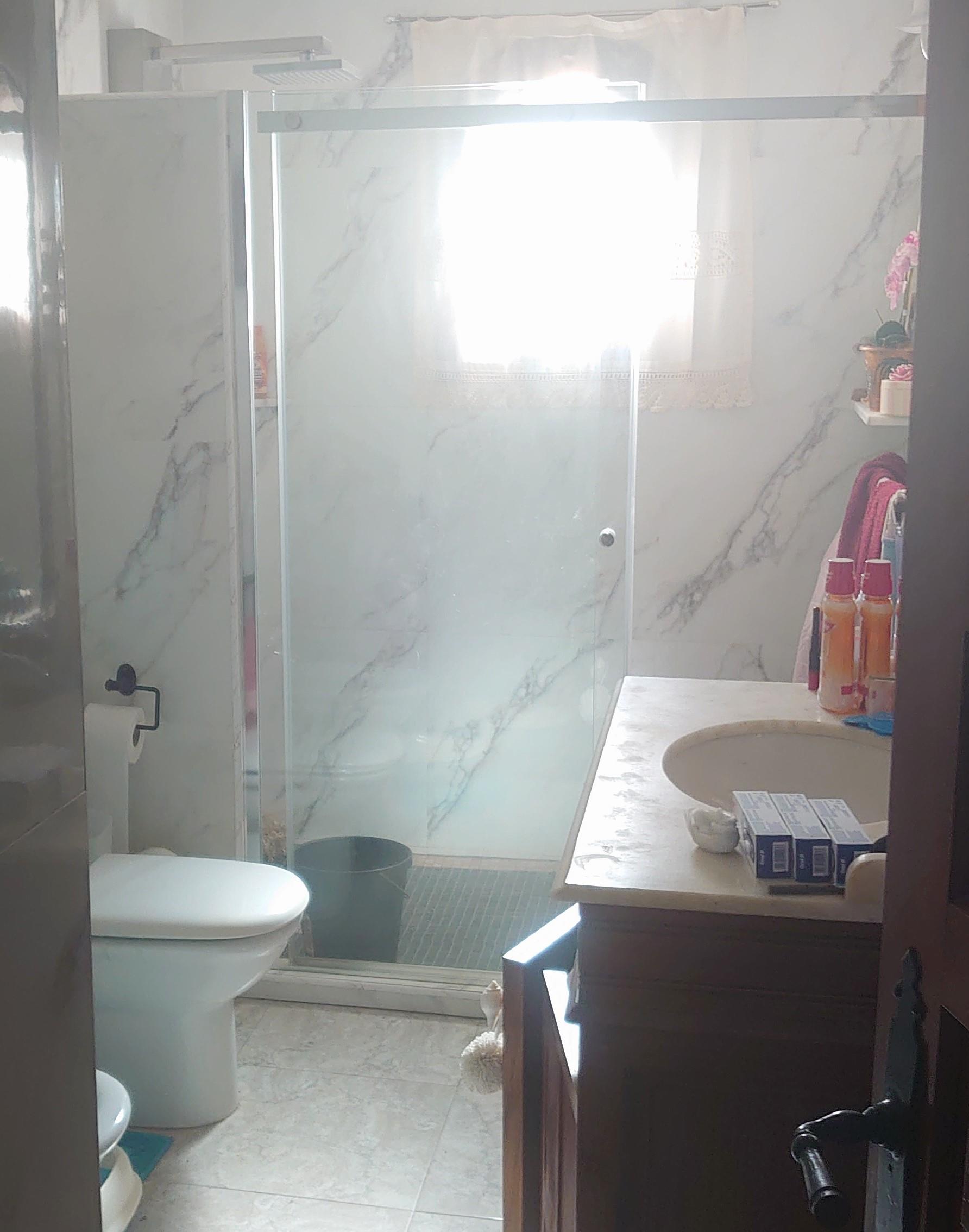 Salle de bain avec carrelage effet marbre, douche à l'italienne avec paroi en verre et meuble vasque en bois avec plan de travail en pierre naturelle.