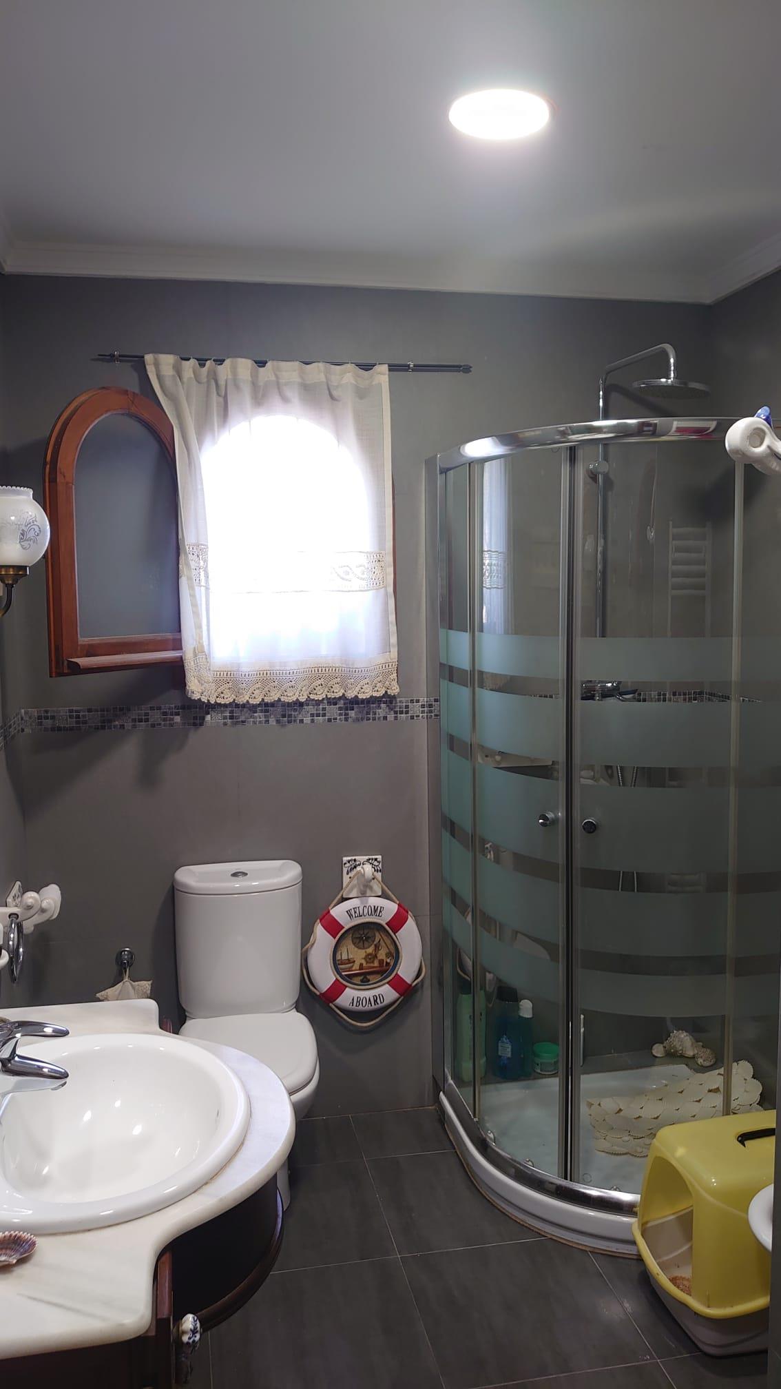 Salle de bain avec douche d'angle vitrée, murs gris et plan de vasque en marbre. Elle comprend une fenêtre à arc en bois et une décoration aux accents nautiques.
