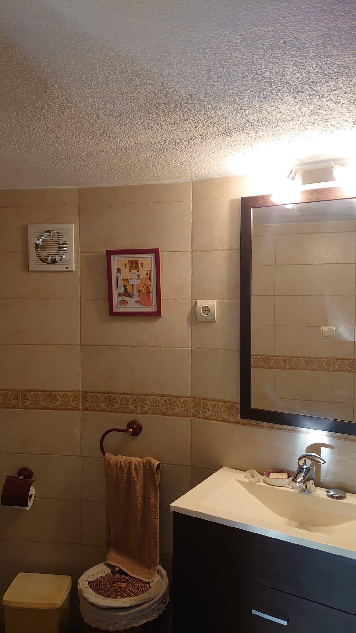 Salle de bain fonctionnelle avec meuble sous-vasque sombre, miroir encadré et murs carrelés beige agrémentés d'une frise décorative.